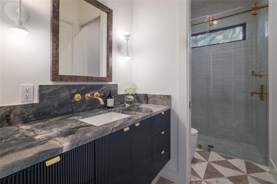The first floor guest bathroom was designed to wow! The Ijen Blue countertop and sumptuous deep navy high-sheen lacquered cabinetry are offset with bright brass hardware and plumbing and a striking patterned marble floor....