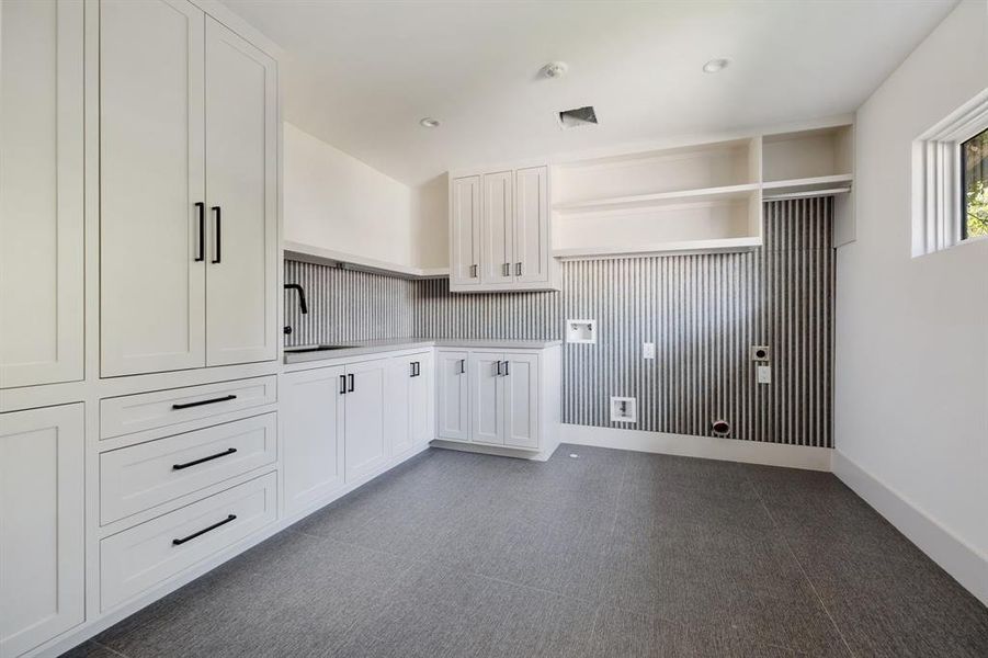 The efficient second floor laundry room features a delicates-friendly sink and abundant storage and work space. Windows fill the space with natural light, complementing the Porcelanosa floor tile and backsplash. Adjacent linen storage (elevator shaft), adds further practicality to this well-designed room.