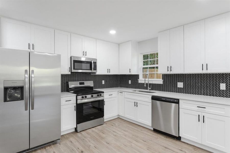 Kitchen with tasteful backsplash, sink, white cabinetry, light hardwood / wood-style flooring, and appliances with stainless steel finishes