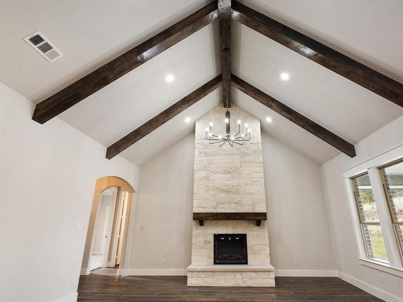 Unfurnished living room with lofted ceiling with beams, a chandelier, dark wood-type flooring, and a stone fireplace