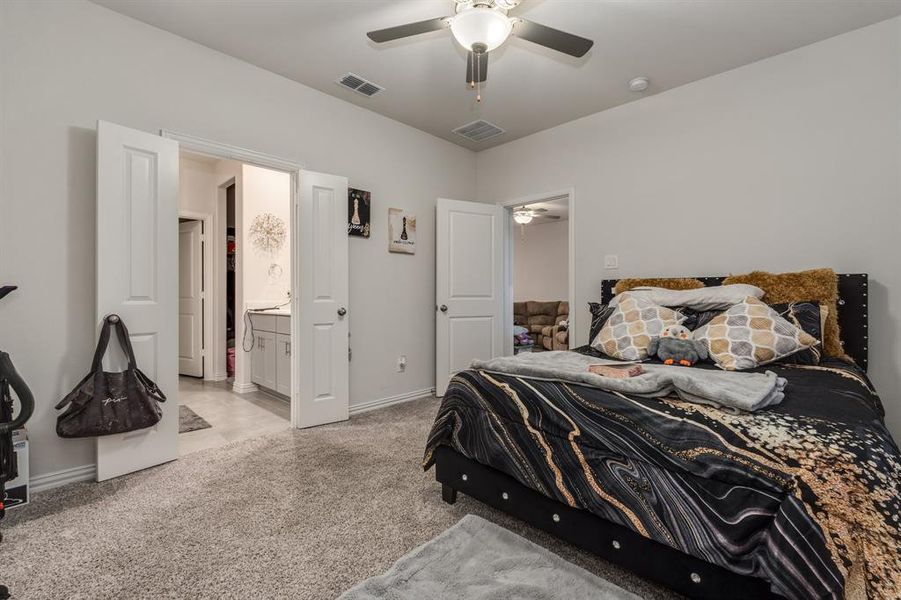 Carpeted bedroom featuring ensuite bath and ceiling fan