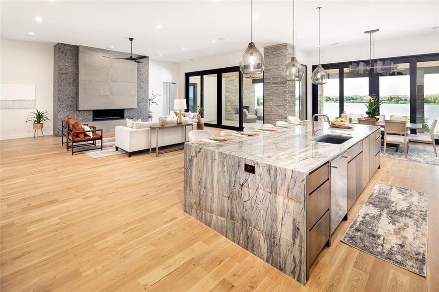 Kitchen featuring light stone counters, light wood-type flooring, a large island with sink, sink, and dishwasher