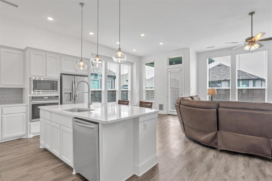 Kitchen featuring light hardwood / wood-style flooring, stainless steel appliances, pendant lighting, decorative backsplash, and an island with sink