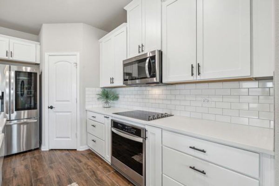 Kitchen with appliances with stainless steel finishes, decorative backsplash, white cabinets, and dark wood-type flooring