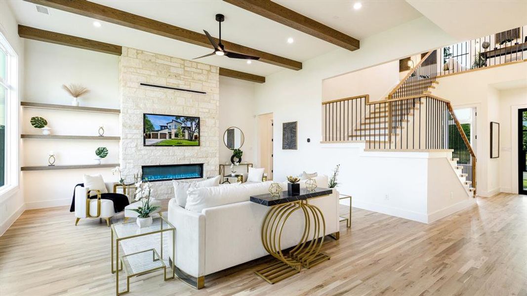 Living room featuring a fireplace, a towering ceiling, light wood-type flooring, and ceiling fan