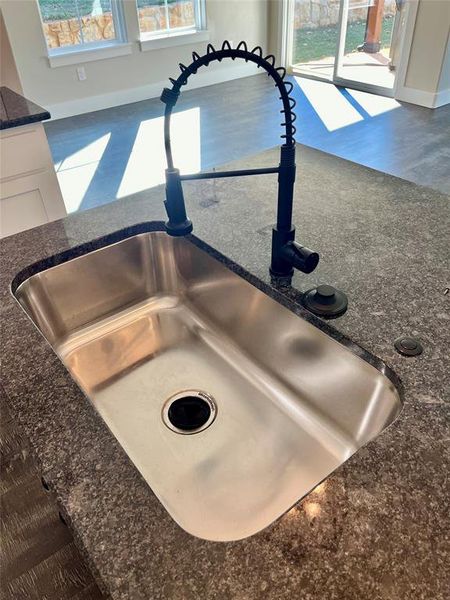 Details featuring white cabinetry, sink, dark stone counters, and hardwood / wood-style floors