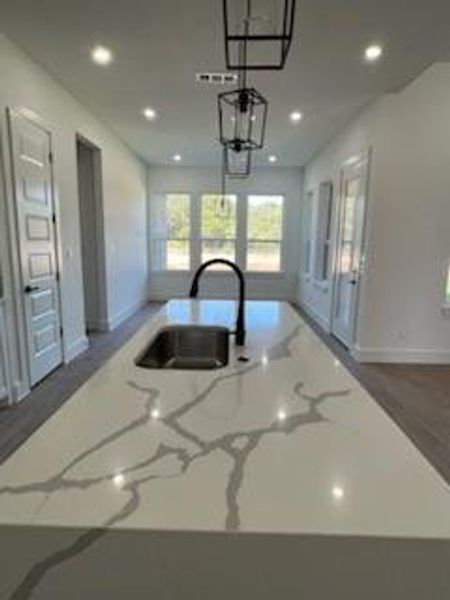 Kitchen with pendant lighting, dark hardwood / wood-style flooring, a center island with sink, sink, and light stone countertops