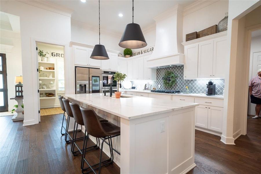 Kitchen featuring, white cabinets and decorative hanging lights fixtures, a kitchen island with sink, dark wood-type flooring, white cabinetry, and stainless steel appliances