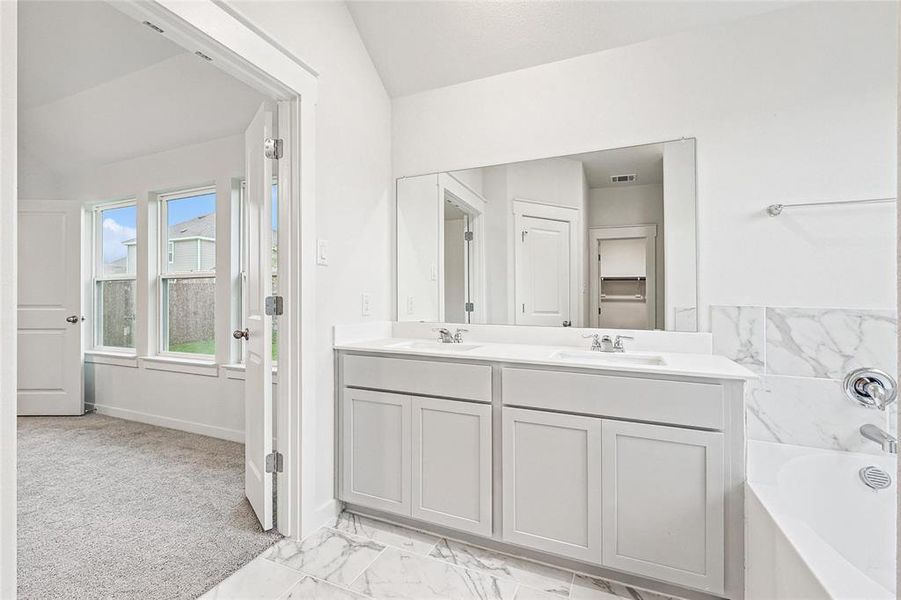 Bathroom featuring tile patterned floors, double sink vanity, a bathing tub, and vaulted ceiling