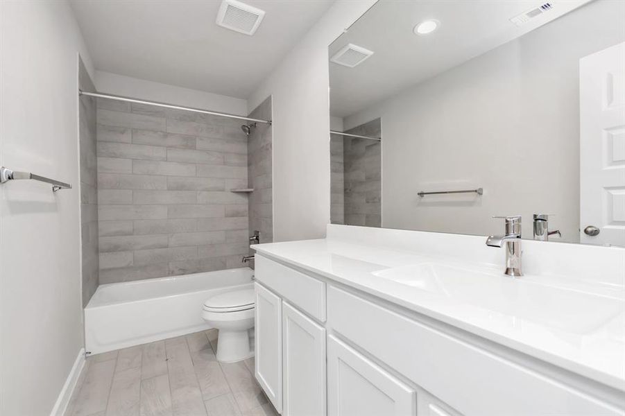 Indulge in refined charm in the secondary bathroom, where the tile flooring harmonizes with a bath/shower combo surrounded by tasteful tile. Light wood cabinets, coupled with a gorgeous countertop, elevate the space, cultivating a truly welcoming atmosphere. Sample photo of completed home with similar floor plan. As-built interior colors and selections may vary.