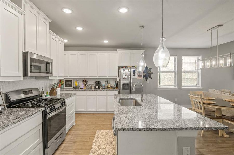 Kitchen with white cabinets, pendant lighting, sink, appliances with stainless steel finishes, and light hardwood / wood-style flooring