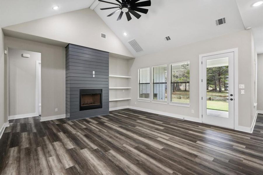 Unfurnished living room with dark wood-type flooring, built in shelves, high vaulted ceiling, ceiling fan, and a fireplace