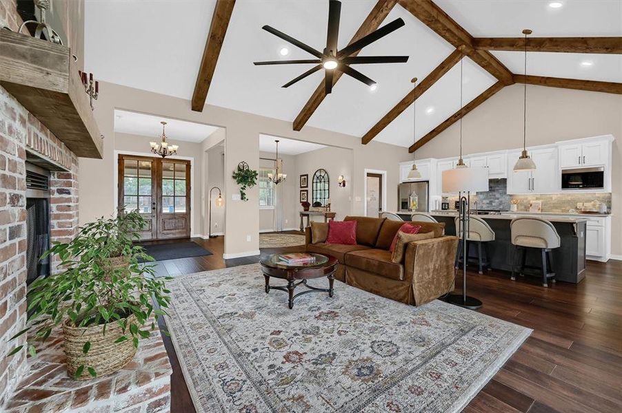 Living room with beam ceiling, dark hardwood / wood-style flooring, high vaulted ceiling, a brick fireplace, and ceiling fan