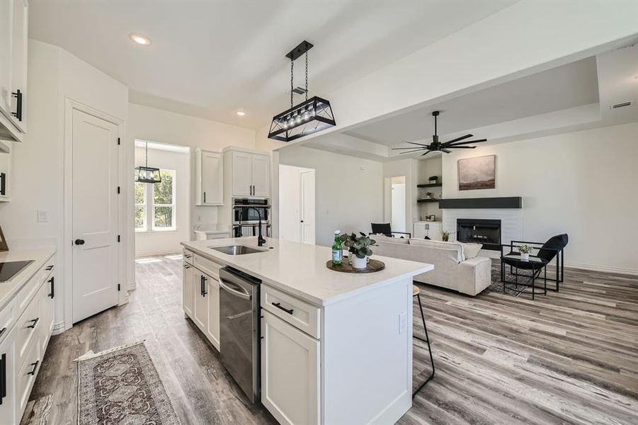 Kitchen with white cabinetry, ceiling fan with notable chandelier, pendant lighting, a center island with sink, and sink