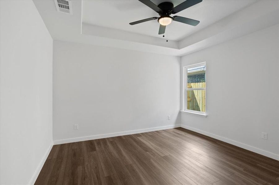 Unfurnished room featuring wood-type flooring, ceiling fan, and a tray ceiling