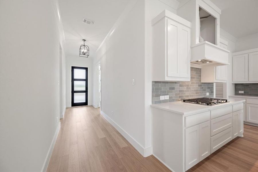 Kitchen with stainless steel gas stovetop, white cabinets, backsplash, premium range hood, and light hardwood / wood-style floors