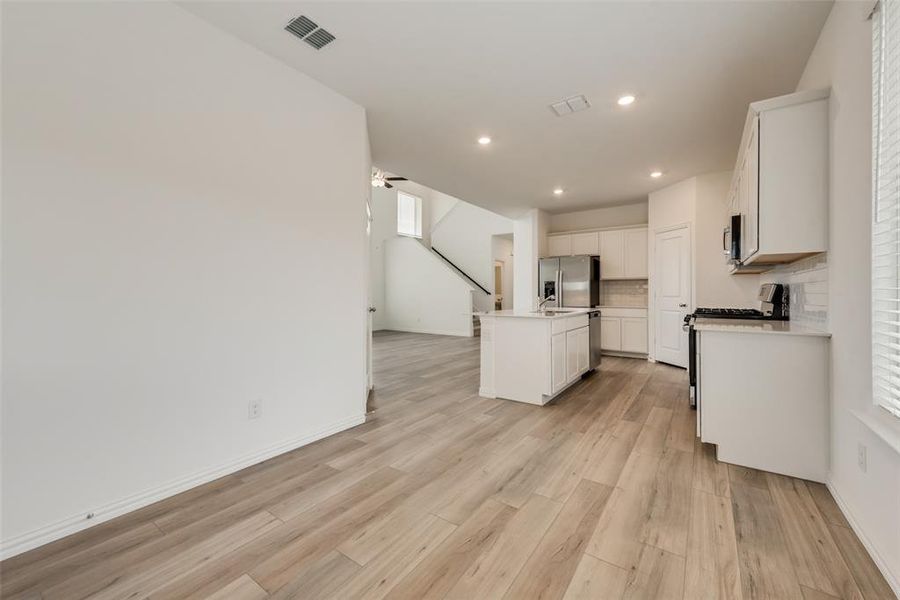 Kitchen featuring appliances with stainless steel finishes, light wood-type flooring, an island with sink, white cabinets, and decorative backsplash