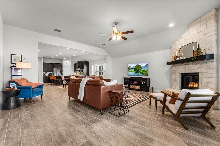 Living room with ceiling fan, a fireplace, vaulted ceiling, and light wood-type flooring