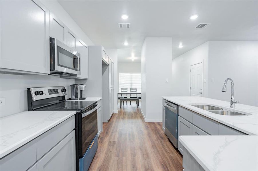 Kitchen with dark hardwood / wood-style flooring, appliances with stainless steel finishes, light stone countertops, gray cabinets, and sink