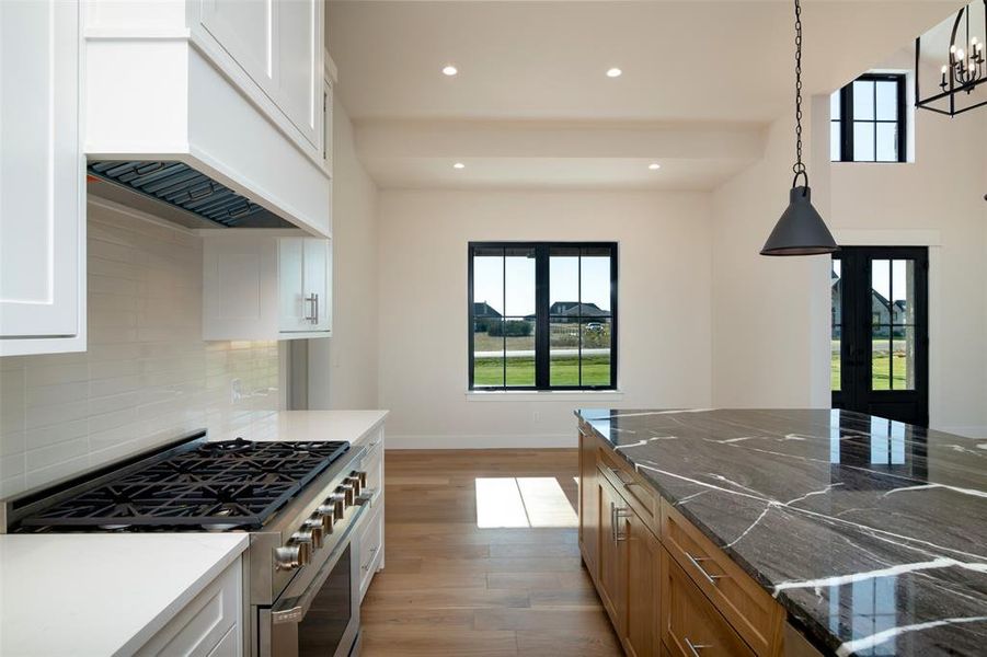 Kitchen featuring white cabinetry, light hardwood / wood-style floors, dark stone counters, stainless steel range, and decorative light fixtures