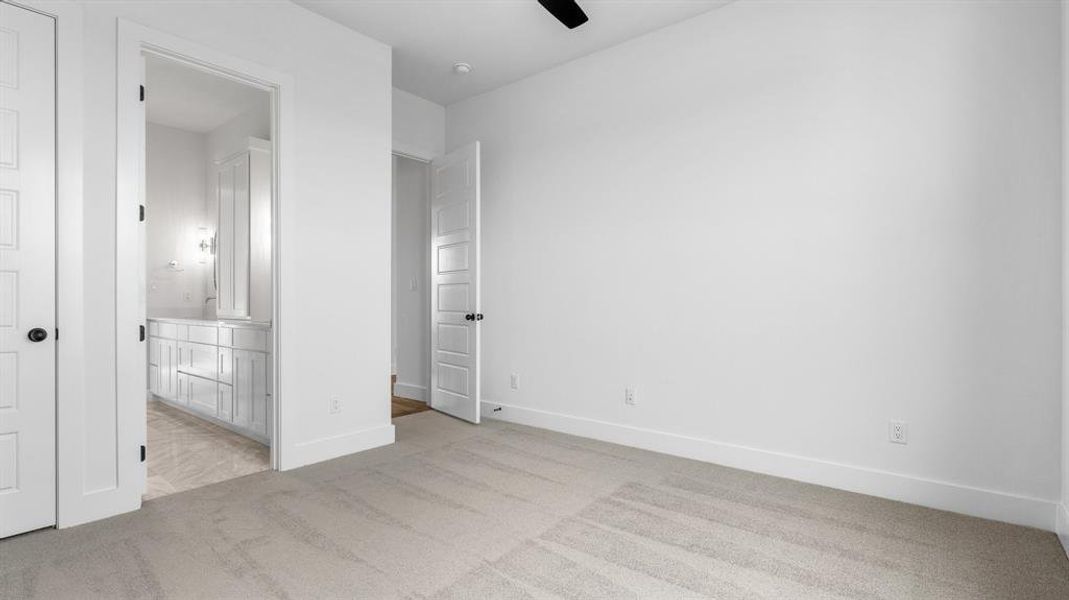 Unfurnished bedroom featuring ceiling fan, light colored carpet, and ensuite bathroom