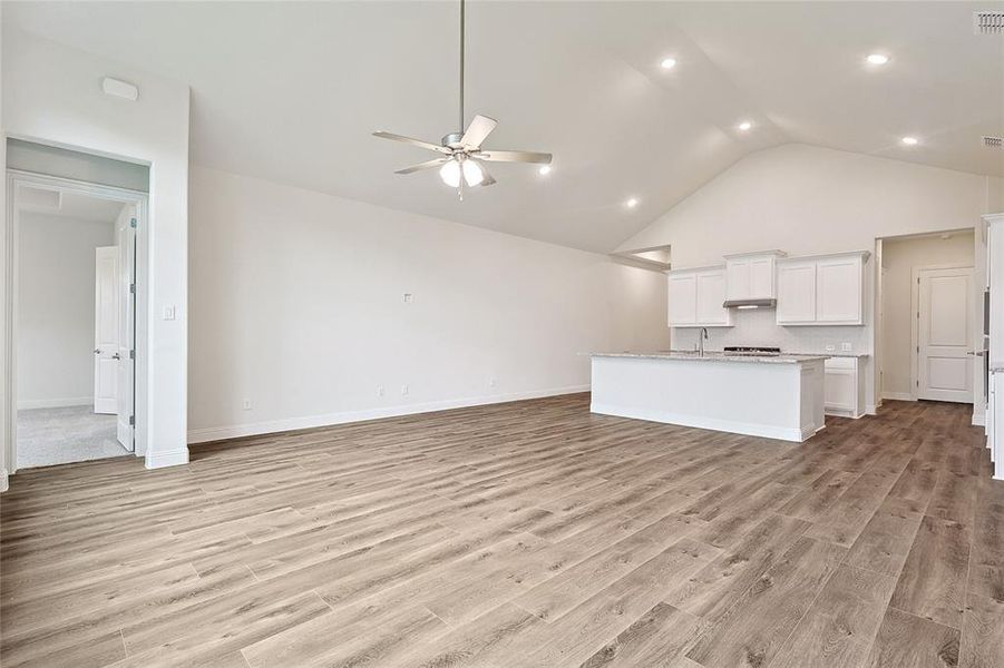 Unfurnished living room with light hardwood / wood-style floors, sink, ceiling fan, and high vaulted ceiling