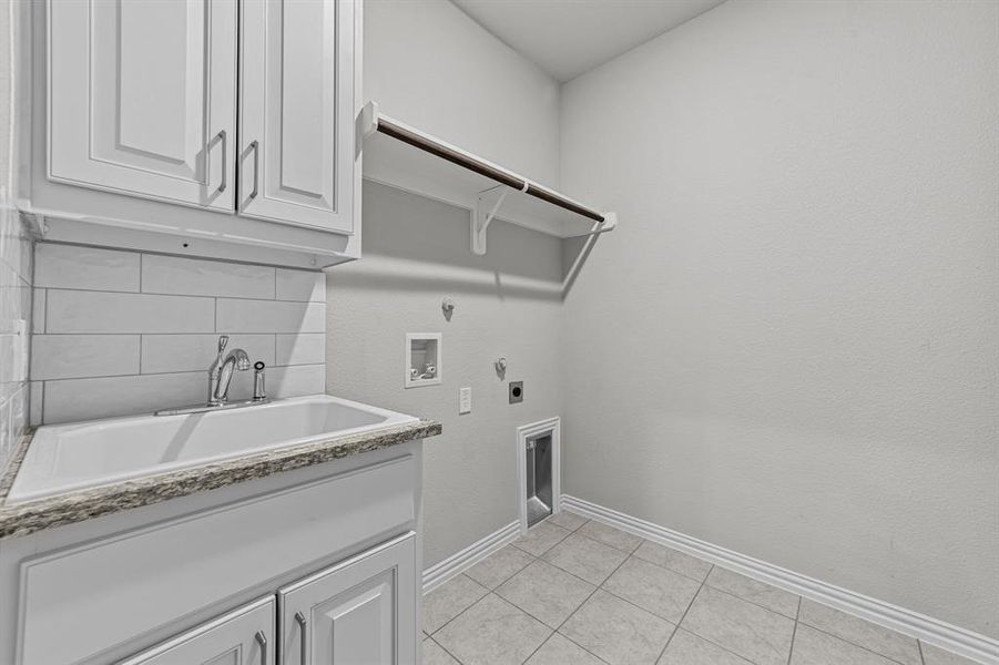 Laundry room featuring cabinets, light tile patterned floors, washer hookup, sink, and hookup for an electric dryer