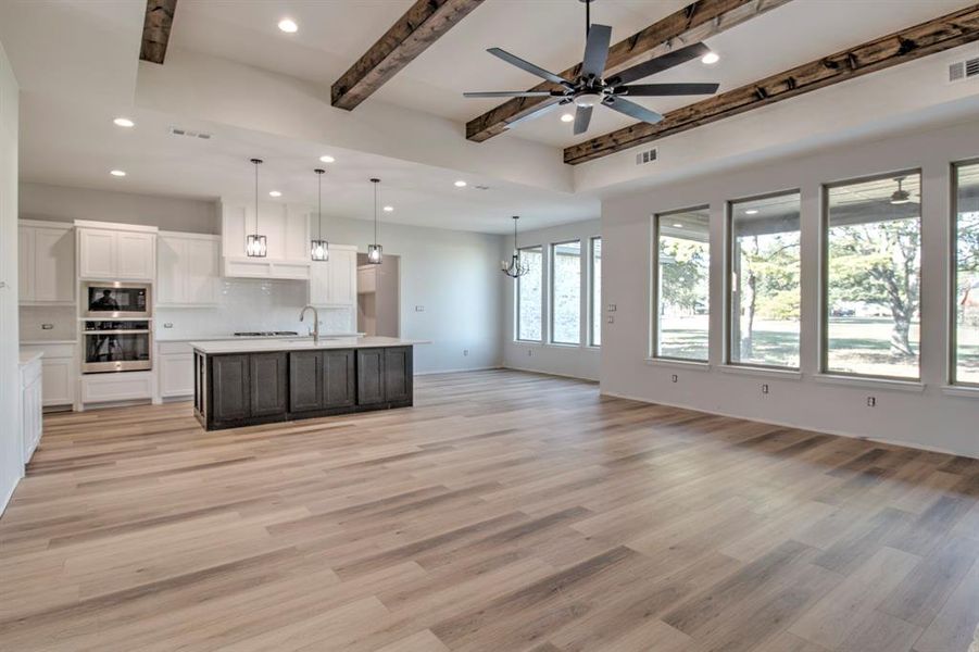 Kitchen featuring an island with sink, white cabinetry, stainless steel appliances, beamed ceiling, and decorative light fixtures