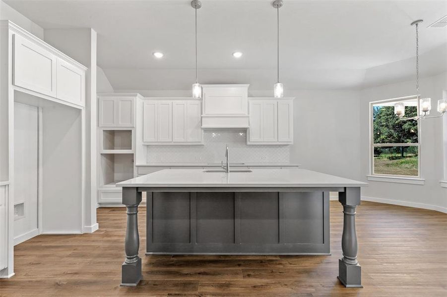 Kitchen with hanging light fixtures, a kitchen island with sink, hardwood / wood-style floors, white cabinetry, and sink