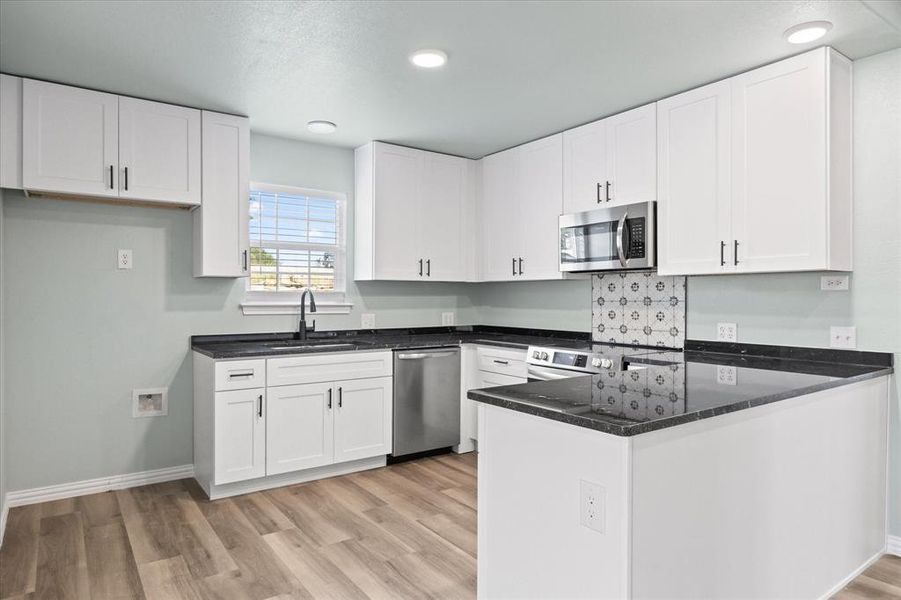 Kitchen with stainless steel appliances, white cabinetry, and sink