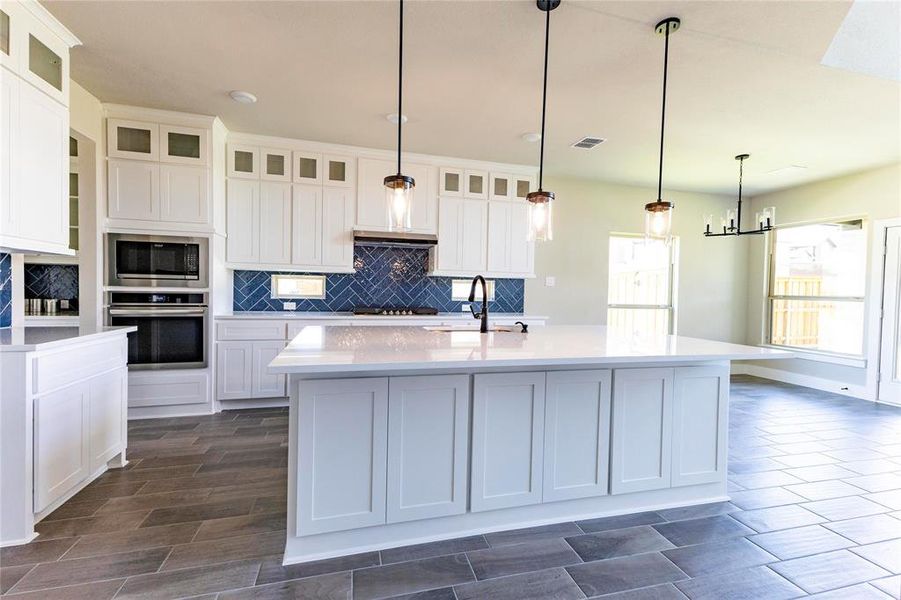 Kitchen with white cabinets, backsplash, a kitchen island with sink, stainless steel appliances, and pendant lighting