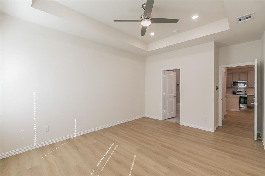 Unfurnished room with a raised ceiling, ceiling fan, and light wood-type flooring