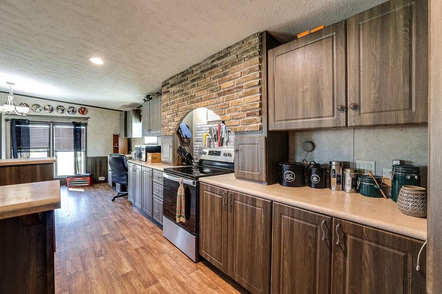 Kitchen featuring stainless steel range with electric stovetop, light hardwood / wood-style floors, dark brown cabinetry, and a textured ceiling