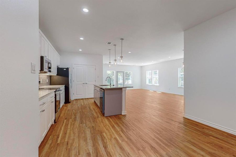 Un-staged Kitchen featuring white cabinets, an island with sink, pendant lighting, appliances with stainless steel finishes, and light hardwood / wood-style floors