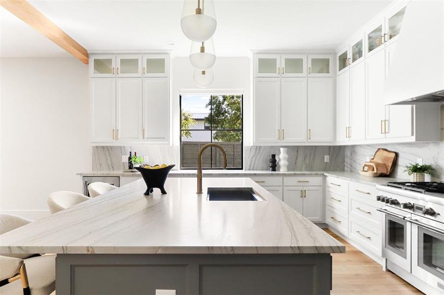 Kitchen featuring premium range hood, a breakfast bar area, range with two ovens, decorative light fixtures, and a center island with sink