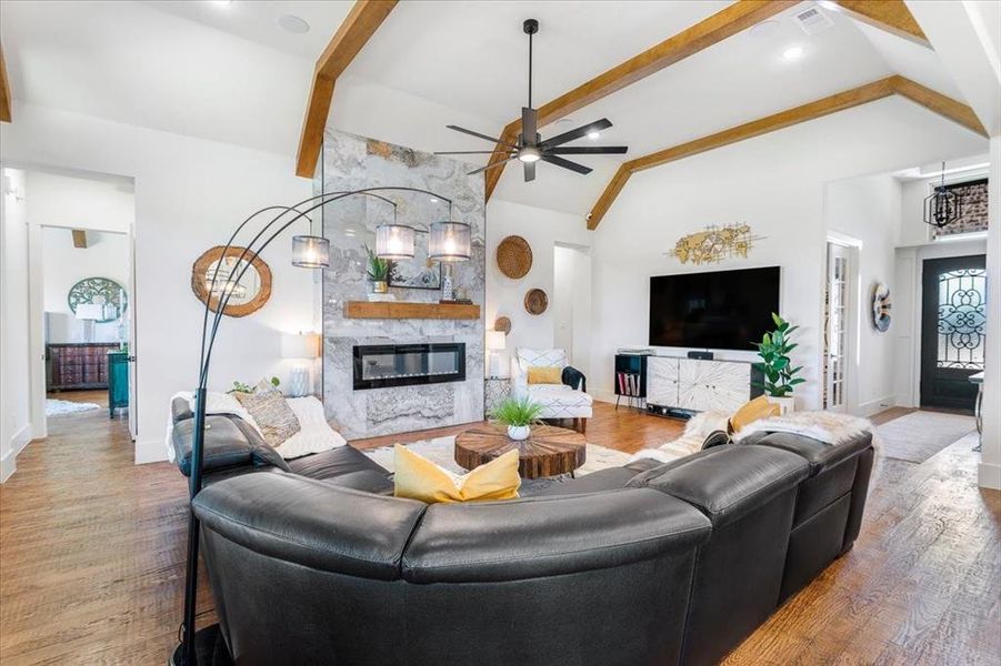 Living room featuring a stone fireplace, ceiling fan, beamed ceiling, and hardwood / wood-style flooring