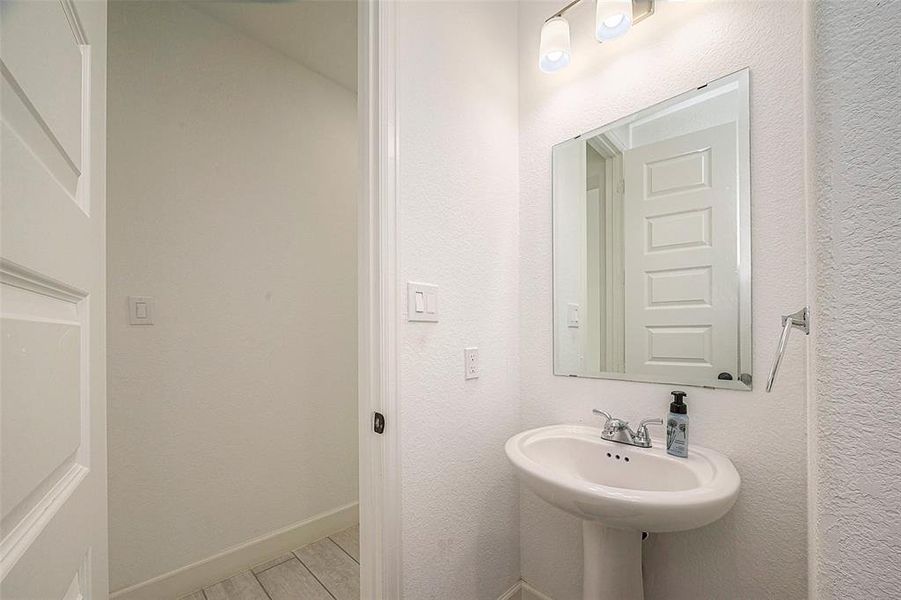 This is a compact, well-lit half-bathroom featuring a pedestal sink, a mounted mirror, modern lighting, and neutral colors, ideal for guest use.