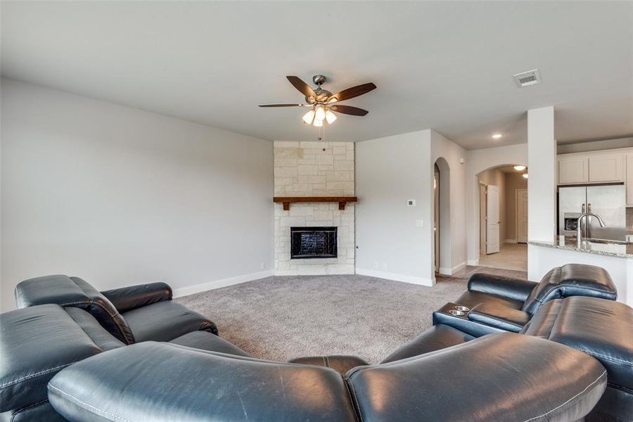 Carpeted living room with ceiling fan, a fireplace, and sink