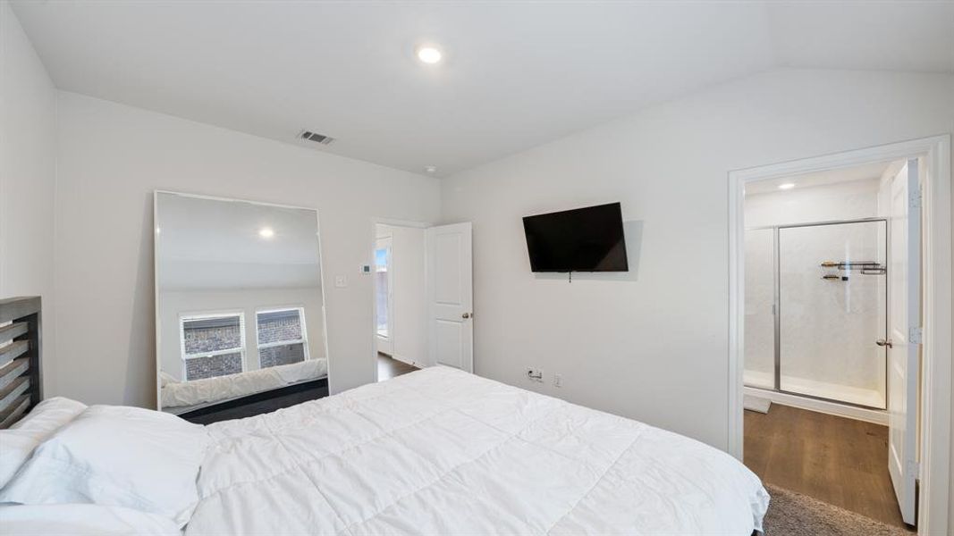 Bedroom with hardwood / wood-style floors, lofted ceiling, and ensuite bath