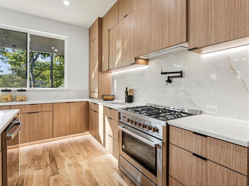 Kitchen with high end stove, tasteful backsplash, and light hardwood / wood-style flooring