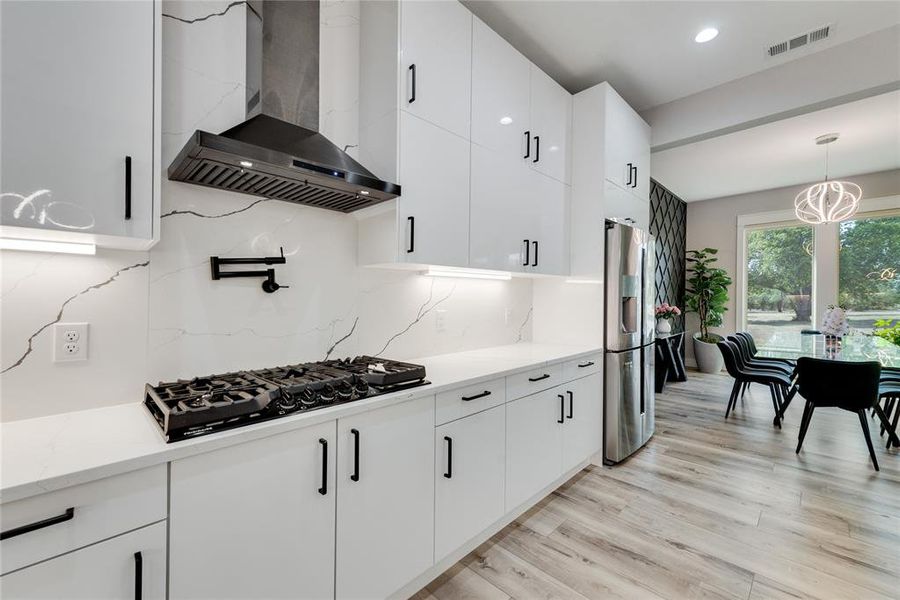 Kitchen featuring backsplash, stainless steel fridge, wall chimney range hood, and white cabinetry