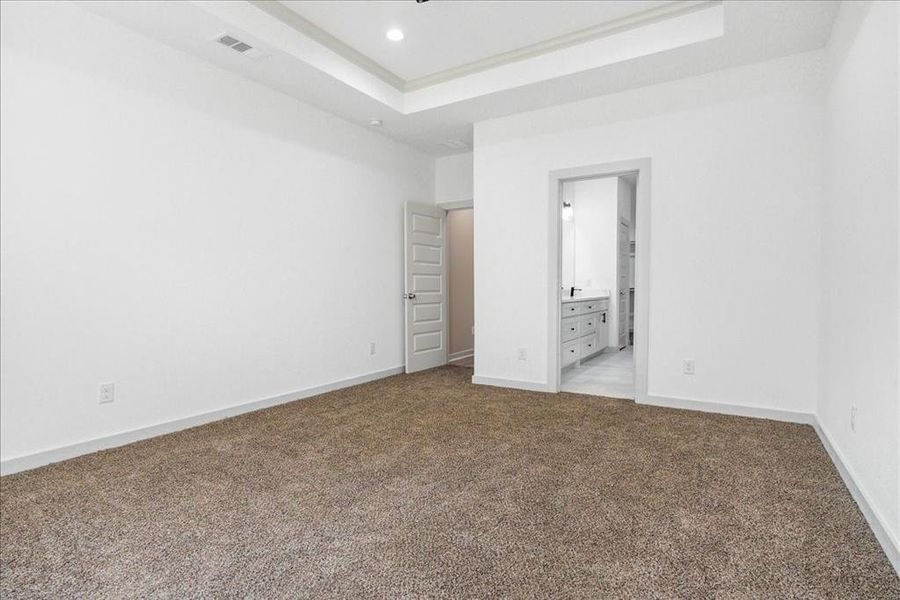 Unfurnished bedroom featuring ensuite bath, light colored carpet, and a tray ceiling