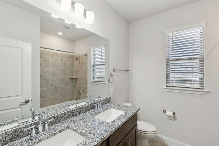 Full bathroom with tiled shower / bath, double sink vanity, and toilet