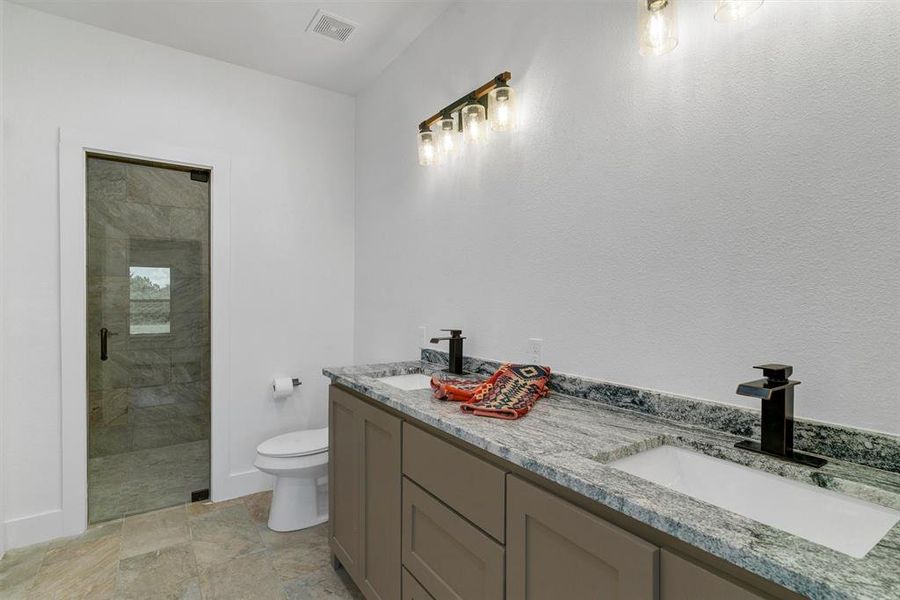 Bathroom with tile floors, dual vanity, a shower with door, and toilet