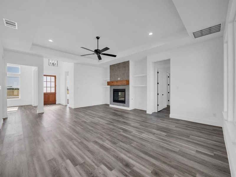 Unfurnished living room with a fireplace, dark hardwood / wood-style floors, a tray ceiling, built in shelves, and ceiling fan