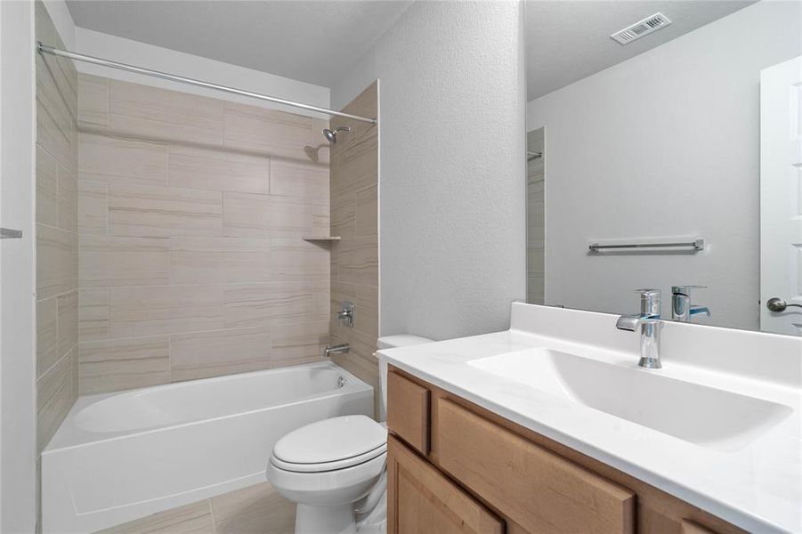 Secondary bath features tile flooring, bath/shower combo with tile surround, wood stained cabinets, beautiful light countertops, mirror, dark, sleek fixtures and modern finishes!