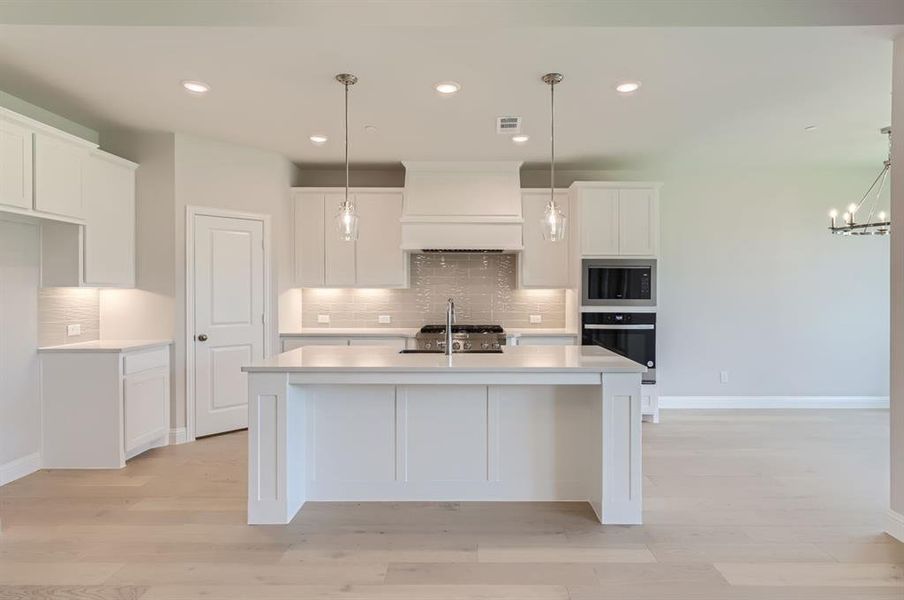 Kitchen featuring decorative backsplash, oven, custom exhaust hood, and a kitchen island with sink