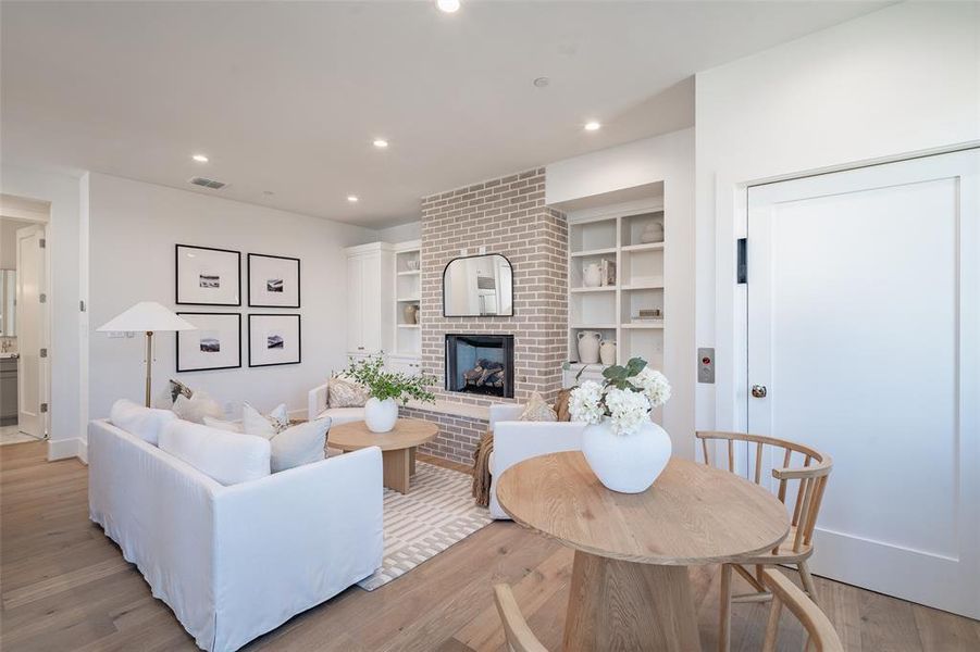 Living room featuring a brick fireplace, built in features, and light hardwood floors