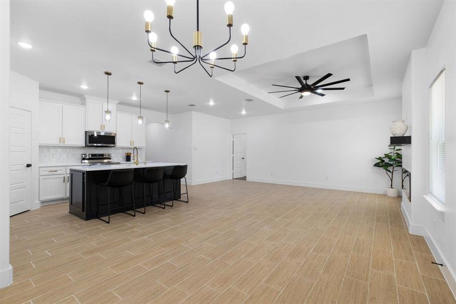Kitchen with ceiling fan with notable chandelier, backsplash, hanging light fixtures, appliances with stainless steel finishes, and a center island with sink