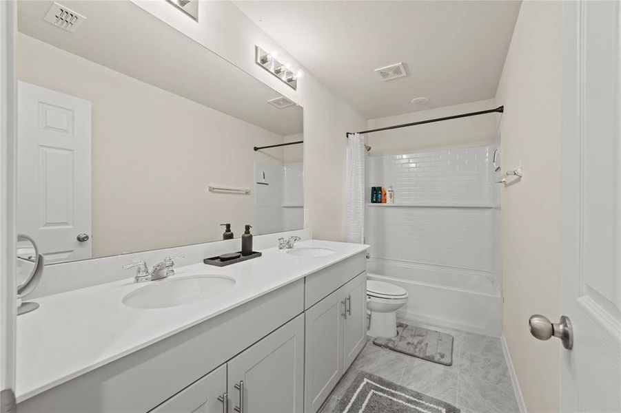 Full bathroom featuring double vanity, tile patterned flooring, toilet, and shower / tub combo